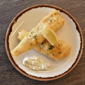 battered haddock goujons with a slice of lemon on top and tartare sauce by the side on a white plate